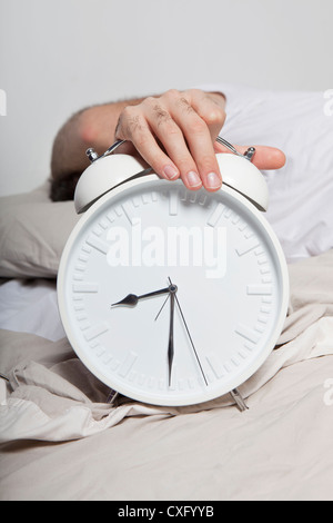 A man laying in a bed and holding a big white alarm clock. Stock Photo