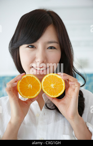 A woman in white shirt holding two oranges in a kitchen Stock Photo