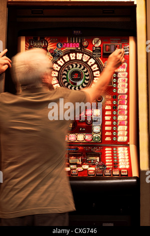 A man approximately 60 years old, (showing slight movement) placing a coin in a slot machine Stock Photo