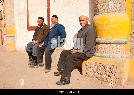 Uighur men sit outside a mosque in a village at the foot of the Flaming Mountains east of Turpan, Xinjiang, China Stock Photo