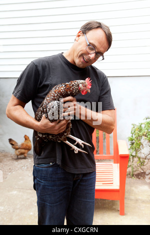 A man is holding a chicken in his backyard. Stock Photo