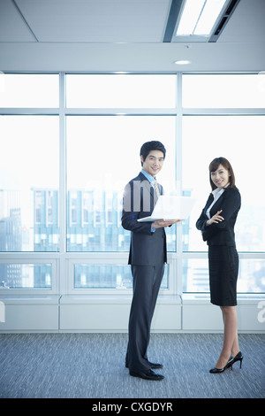 A business woman and a man standing in front of windows while man holding a laptop Stock Photo