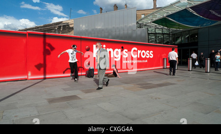 Man in a suit walking past break dancer ouside King's Cross Train Station red sign London England UK  KATHY DEWITT Stock Photo