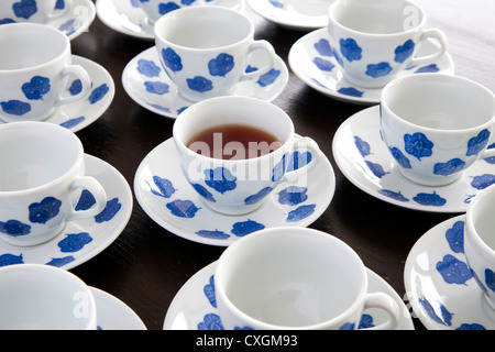 One cup of tea in blue and white teacup, surrounded by empty teacups. Stock Photo