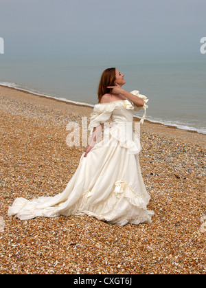 Girl Wearing a Cream White Wedding Dress on a Shingle Beach by the Sea.