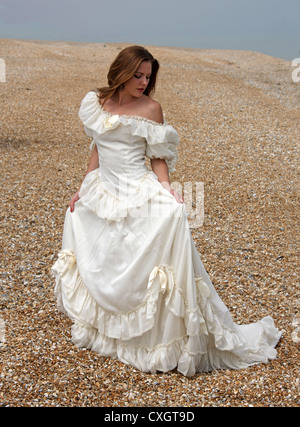 Girl Wearing a Cream White Wedding Dress on a Shingle Beach by the Sea.