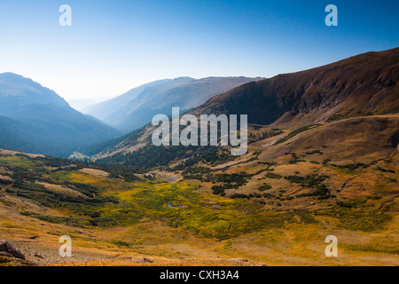 A beautiful valley around the tundra area at Rocky Mountain National Park was seen in the morning sun. Several elks were walking across a stream at the bottom of the valley. Stock Photo