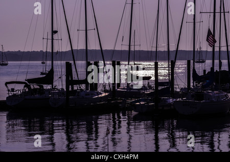 Docked sailboats silhouetted against a purple sky at sunrise. Sunlight shimmers on the water. Niantic East Lyme Connecticut USA Stock Photo