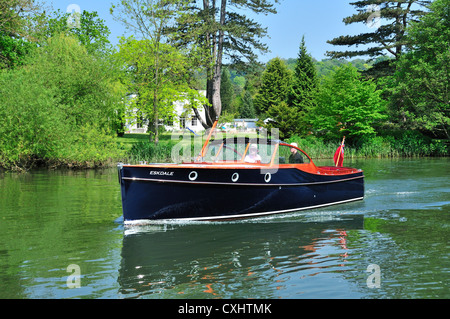 Couple cruising on a gentlemans motor yacht or motorboat on the Upper Reaches of the River Thames at Pangbourne, Berkshire, England, UK Stock Photo