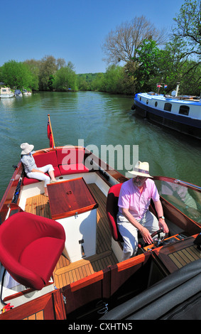 Couple cruising on a gentlemans motor yacht or motorboat on the  upper reaches of the River Thames, Pangbourne, Berkshire, England, UK Stock Photo