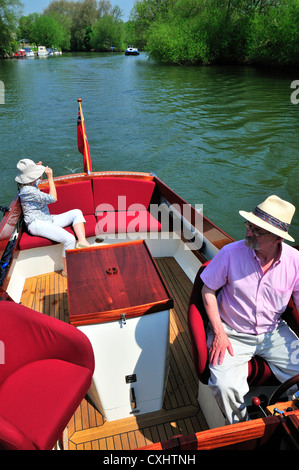 Couple cruising on a gentlemans motor yacht or motorboat on the  upper reaches of the River Thames, Pangbourne, Berkshire, England, UK Stock Photo