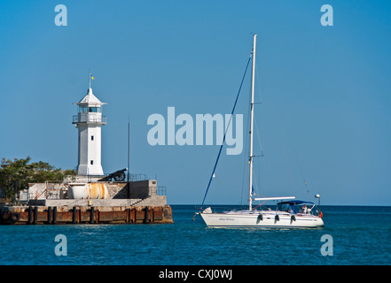 Sailboat passing lighthouse in Yalta harbor Stock Photo