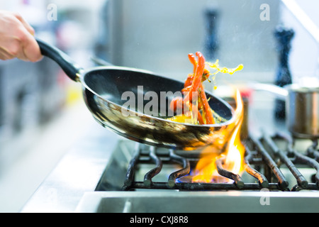 Chef in restaurant kitchen at stove with pan, doing flambe on food Stock Photo