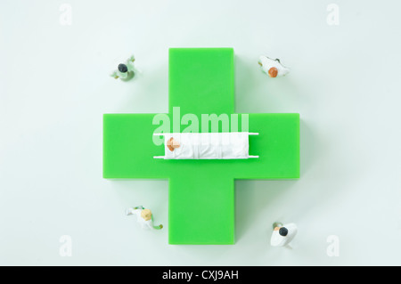 Figurines of doctors and patient with green medical symbol Stock Photo