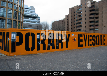 Black and yellow 'TEMPORARY EYESORE' sign on barrier around construction site near Tate Modern Stock Photo