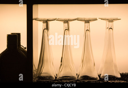 Upturned crystal cocktail glasses on an illuminated shelf in a bar ready for use Stock Photo