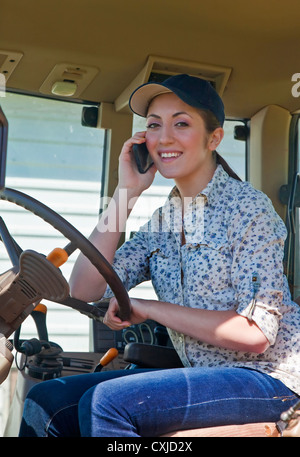 Young woman farmer speaking on her phone in the cab of her tractor. Stock Photo