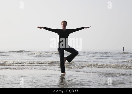 Belgium, Young woman standing in tree pose at North Sea Stock Photo