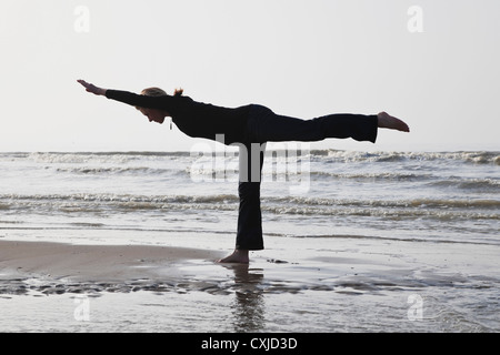 Belgium, Young woman standing in warrior III pose at North Sea Stock Photo