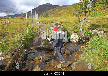 A woman walker and her dog fording a stream in Glen Affric Scottish Highlands Scotland UK Stock Photo