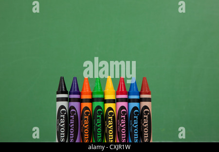 Row of colored crayons on a green chalkboard background with copy space Stock Photo
