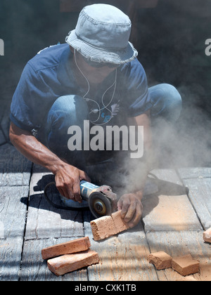 Angle grinder. Builder using a hand powered angle grinder to cut bricks. Thailand S.E. Asia Stock Photo