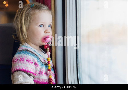 Portrait of Little Girl using Pacifier and Looking out Train Window Stock Photo