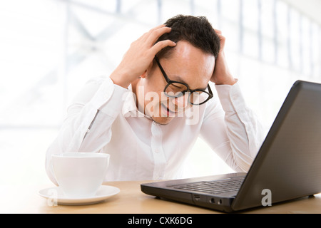 Depressed mid adult Asian business man scratching his head at office Stock Photo