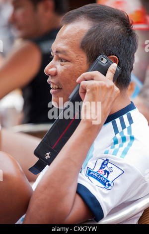 A young Asian man talks on his cell phone while spending time at an outdoor cafe in Sitges, Spain. Stock Photo