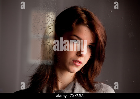 Young woman looking sadly through window glass Stock Photo