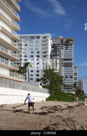 worker cleaning beach raking sand in front of apartments hotels and beachfront developments fort lauderdale beach florida usa Stock Photo