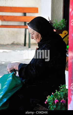 Elderly Greek woman dressed in black  sitting waiting for a bus in the traditional hill village of Kroustas,above Agios Nikolaos, Crete, Greece Stock Photo