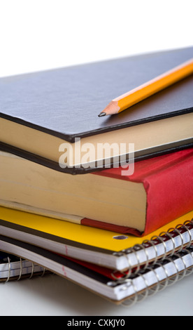 A stack of school books and spiral notebooks with a pencil and pens on tops in front of a white background Stock Photo