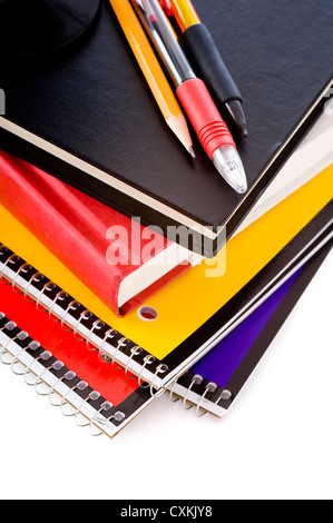 A stack of school books and spiral notebooks with a pencil and pens on tops in front of a white background Stock Photo