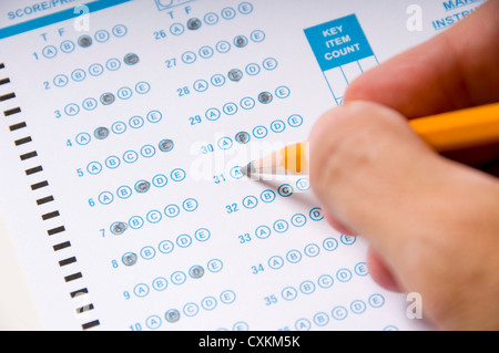 A hand holding a yellow pencil filling in a computer checked answer sheet on an examination. Education concept Stock Photo