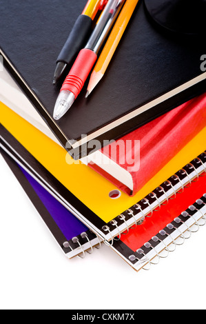 A stack of school books and spiral notebooks with a pencil and pens on tops in front of a white background Stock Photo
