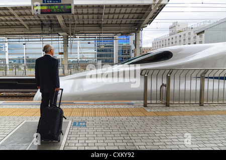 A passenger waits on a station platform as a bullet train arrives. Stock Photo