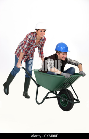 Two female construction workers racing in a wheelbarrow. Stock Photo