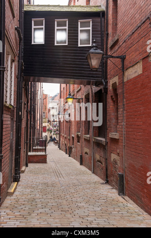 View down narrow enclosed alleyway, lined with high brick walls & glass lanterns to historic inn - Ship Yard, Leeds city centre, West Yorkshire, UK. Stock Photo