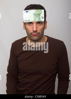 Portrait of sad looking young man with 100 euro bill on forehead Stock Photo