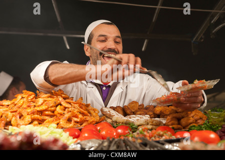 happy local serving up food in food stand market evening Jamaa el Fna Square in Marrakech, Morocco Stock Photo