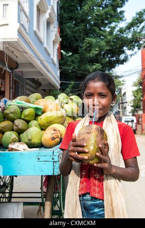 Happy young Indian street girl drinking coconut water from the coconut on a street in India Stock Photo