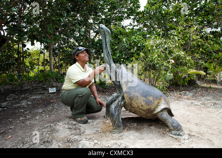 Eco-tour guide squatting beside a bronze statue of an extinct Rodrigues giant tortoise (Cylindraspis vosmaeri), Mauritius Stock Photo