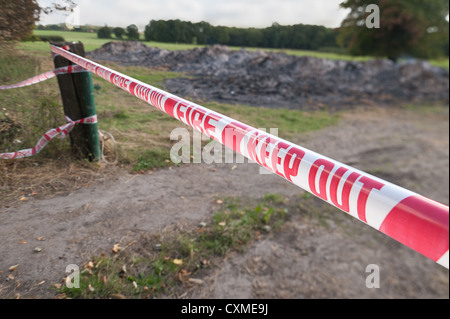 Warning barrier to keep people away from smoldering fire remains cordon off line under tension at waist height tied to post Stock Photo