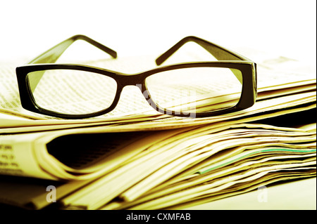 A pair of black reading glasses on top of a stack of newspapers on a white background Stock Photo