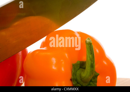 Red and orange bell peppers on cutting board with knife against white background Stock Photo