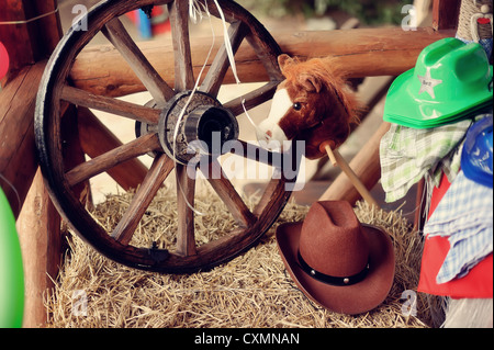 on a haystack the brown cowboy's hat and a wooden wheel lies Stock Photo