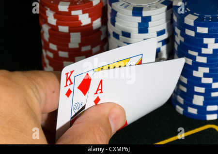 Man's hand holding two playing card while gambling with several denominations of poker chips in the background Stock Photo