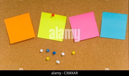 Blank sticky notes on a brown corkboard or bulletin board with colored push pins. add your own text Stock Photo