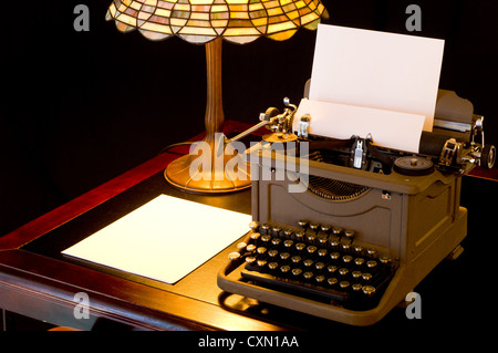 Old, antique, vintage, typewriter in writer's or author's area with lamp on black background Stock Photo